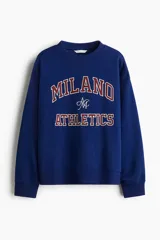 Buzo azul marino de corte oversize con hombros caídos y cuello redondo. Presenta un diseño estampado en el pecho con el texto "Milano Athletics" en color bordó con borde blanco y un monograma central en blanco. Cuenta con ribetes acanalados en el cuello, los puños y el dobladillo inferior.
