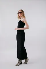 Vestido midi negro ajustado, con tirantes finos, escote recto y detalle de frunce en el lateral del busto. Presenta una abertura lateral en la falda.