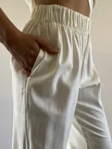 Conjunto de dos piezas compuesto por una remera de corte recto y cuello redondo, y un pantalón de tiro medio con cintura elástica. Ambas prendas están confeccionadas en lino de color manteca.