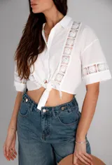 Camisa de manga corta color negro, con cuello camisero, cierre frontal con botones y detalles de encaje bordado en la parte delantera y en las mangas.