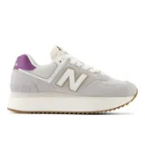Championes urbanos New Balance modelo 574, color gris claro con detalles en blanco y violeta, confeccionados en gamuza y malla, con logo "N" característico en los laterales, plataforma alta y entresuela ENCAP.