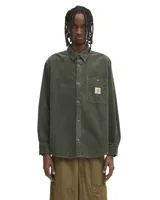 Camisa de manga larga Carhartt modelo Flint, confeccionada en pana de algodón color verde oliva. Presenta cuello clásico, cierre frontal con botones, puños abotonados y un bolsillo en el pecho con etiqueta de la marca.