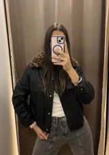 Campera negra de cuero sintético, con cuello de piel sintética con estampado animal print, cierre frontal con botones a presión, bolsillos con solapa en el pecho y corte recto.