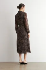 Vestido camisero largo con estampado animal print tipo cebra, en tonos marrón y negro, con cuello camisero, mangas largas y cierre frontal con botones. Incluye un cinturón fino de cordón negro.