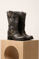 Bota de caña media de cuero color marrón oscuro, con diseño slouchy, hebillas metálicas decorativas y tachas alrededor del tobillo y en la parte superior. Cuenta con taco bajo y cuadrado.