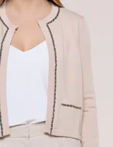 Cardigan corto azul marino de punto, con silueta entallada y largo a la cintura. Cuenta con un ribete decorativo que recorre el cuello redondo y la abertura frontal, integrando una cadena dorada en contraste. Posee bolsillos delanteros simulados y mangas largas.