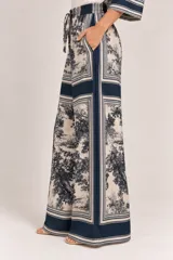 Palazzo amplio de seda con estampado paisajístico y bordes en tono azul marino. Cuenta con cintura elástica con cordón ajustable y bolsillos laterales.