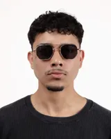 Lentes de sol con montura octogonal dorada y lentes oscuros.