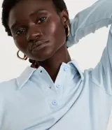 Blusa tipo polo de manga larga, confeccionada en tejido interlock de algodón y poliéster. Presenta cuello clásico con cierre frontal de botones y diseño básico liso.