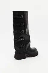 Bota de caña alta estilo biker, color negro, con plataforma robusta y suela dentada. Presenta múltiples tiras laterales con hebillas metálicas ajustables.