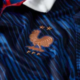 Camiseta de fútbol Nike de la Selección de Francia, modelo local 2026. Presenta un diseño de rayas diagonales en tonos azul oscuro y azul brillante, con cuello tipo polo en color blanco y detalles en rojo. Incluye el logo de Nike y el escudo de la federación francesa en color naranja.