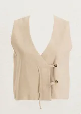 Chaleco de lino con escote en V profundo y cierre frontal cruzado mediante dos botones y tiras de ajuste. Diseño sin mangas y corte recto.