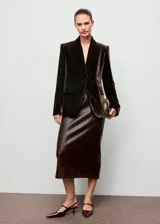 Blazer de corte recto confeccionado en tejido de terciopelo color marrón oscuro. Presenta cuello con solapas de muesca, cierre frontal con un botón, mangas largas con puños abotonados y dos bolsillos laterales con solapa. Incluye forro interior.