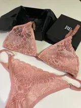 Conjunto de lencería de encaje en color rosado, compuesto por un corpiño triangular sin aro y una bombacha tipo colaless con tiras laterales ajustables.