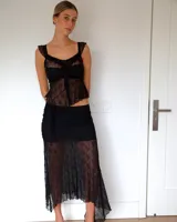 Falda midi de encaje negro con diseño asimétrico y transparencias, que presenta una base opaca corta y una capa superpuesta de encaje largo.