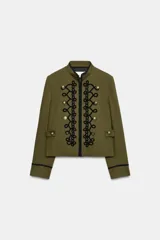 Blazer de estilo militar confeccionado en algodón, con cuello subido y manga larga. Presenta un diseño estructurado con detalle de alamares negros a contraste en el frente, botones metálicos decorativos y trabillas laterales. Cuenta con cierre frontal oculto y forro interior.