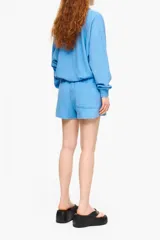 Bermuda celeste de tejido de toalla con corte recto, pierna amplia, cintura elástica y bolsillos laterales. Tiene un pequeño bordado de un perro en la pierna derecha.