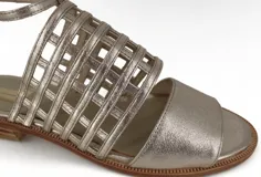 Sandalias doradas de cuero metalizado, con tiras entrecruzadas en el empeine y pulsera con hebilla al tobillo.