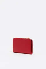 Billetera compacta de cuero vacuno color negro, con cierre superior metálico dorado y logo de la marca estampado en el frente.