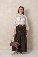 Camisa de organza con bordados florales, cuello camisero, cierre frontal con botones y mangas largas. Presenta un diseño traslúcido y ligero.