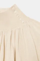 Blusa marrón de punto fluido, con cuello subido abotonado en un lateral y mangas largas con puños ajustados. Presenta un diseño fruncido en la parte frontal que aporta volumen.