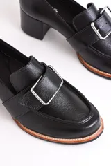 Mocasín negro de cuero con hebilla metálica plateada y taco cuadrado.