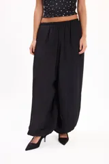 Pantalón negro de corte holgado y fluido, tipo bombacho, con cintura elástica fruncida y botamangas ajustadas.
