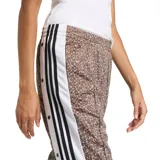 Pantalón Adidas Adibreak de corte holgado, confeccionado en poliéster reciclado con estampado animal print tipo jirafa en tonos marrón y blanco. Cuenta con bandas laterales blancas con líneas negras y botones a presión, además del logo clásico de la marca.