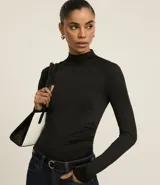 Blusa negra de mangas largas, con cuello alto y fruncidos delanteros.