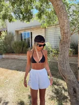 Conjunto de bikini negro con corpiño triangular con argolla metálica y bombacha colaless con tiras para atar y argollas en los costados.