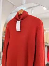 Polera de cuello alto en color terracota, confeccionada con un interior suave y cálido. Presenta puños y ruedo acanalados, con un pequeño aplique metálico decorativo en la parte inferior.