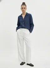 Camisa de denim color azul medio, de manga larga y cuello clásico. Presenta cierre frontal de botones y un bolsillo superior en el lado izquierdo del pecho. Corte regular.