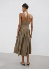 Vestido midi de corte evasé con estampado de cuadros vichy en tonos marrón y blanco. Presenta escote halter con tirantes finos para anudar al cuello, detalle fruncido en el centro del pecho y falda amplia de largo midi.