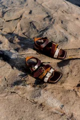 Sandalias de cuero marrón con diseño de tiras múltiples, hebillas metálicas ajustables y detalle de cuero con pelo estampado en la parte frontal. Presentan una base cuadrada y cierre de pulsera en el tobillo.