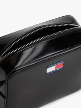 Cartera tipo bandolera de Tommy Jeans con acabado brillante y liso. Presenta un compartimento principal con cierre de cremallera y una insignia con el logo de la marca en la parte frontal. Incluye una correa ajustable.