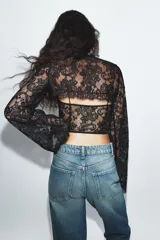 Top de encaje negro con cuello alto, mangas largas acampanadas, corsé interior estructurado y bajo asimétrico.