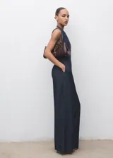 Mono largo de denim oscuro con cuello halter y espalda descubierta. Presenta un diseño de corte recto y holgado con bolsillos laterales y cierre de cremallera en la parte posterior.