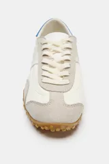 Zapatilla deportiva estilo blucher de color blanco, con detalles en gris claro, una franja lateral blanca y una talonera azul. Cuenta con cordones, punta redonda y suela de goma con tachuelas.