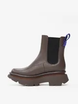 Bota tipo Chelsea de cuero de oveja color marrón, con paneles elásticos laterales negros y suela chunky dentada. Incluye un tirador trasero con detalle tejido en azul.