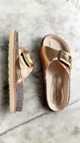 Sandalias de cuero dorado marca Carolina De Cunto, con tira ancha ajustable mediante hebilla metálica grande personalizada y detalles pintados a mano. Suela de goma eva ligera.
