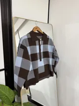 Sweater de punto con diseño de cuadros grandes en tonos marrón y celeste, con cuello polo y cierre frontal de botones.