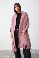 Chal de tejido de punto con textura acanalada, color rosa, con terminación de flecos en los extremos y etiqueta de cuero con logo de la marca.