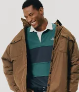 Remera tipo chomba de manga larga, con bloques de color en tonos verde y azul marino, cuello polo blanco y pequeño bordado en el pecho.