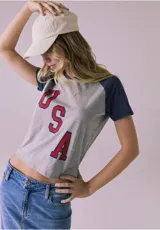 Remera gris de manga corta con mangas ranglán azul marino y estampa frontal con las letras "USA" en rojo con borde azul.