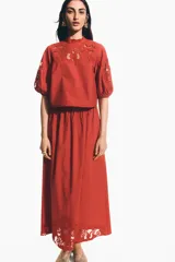 Blusa de viscosa color rojo óxido con secciones de broderie en el pecho y las mangas, cuello elevado festoneado y mangas globo al codo con puños elásticos.