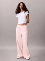 Pantalón de felpa francesa rosa pastel, de corte holgado con basta ancha y tiro medio. Posee cintura elástica, bolsillos laterales y una pequeña insignia blanca con el logotipo de Calvin Klein en el lateral izquierdo.