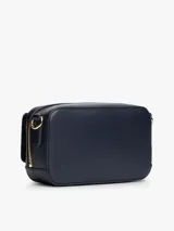 Cartera tipo cámara estructurada de color azul marino, con solapa frontal y logo metálico de Tommy Hilfiger en dorado. Posee un bolsillo externo con cierre de solapa a broche y correa ajustable extraíble.