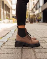 Borcego de gamuza color chocolate con paneles laterales elásticos negros y suela track dentada. Presenta sistema de cordones con ganchos metálicos y tirador en la parte trasera.