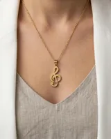 Dije con forma de clave de sol, elaborado en acero con baño dorado, con textura punteada en su superficie.