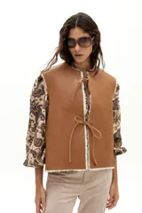 Chaleco reversible de gamulán de oveja en color natural, con corte holgado, cuello a la base y terminaciones al corte. Presenta tiras de cuero en el frente para atar.